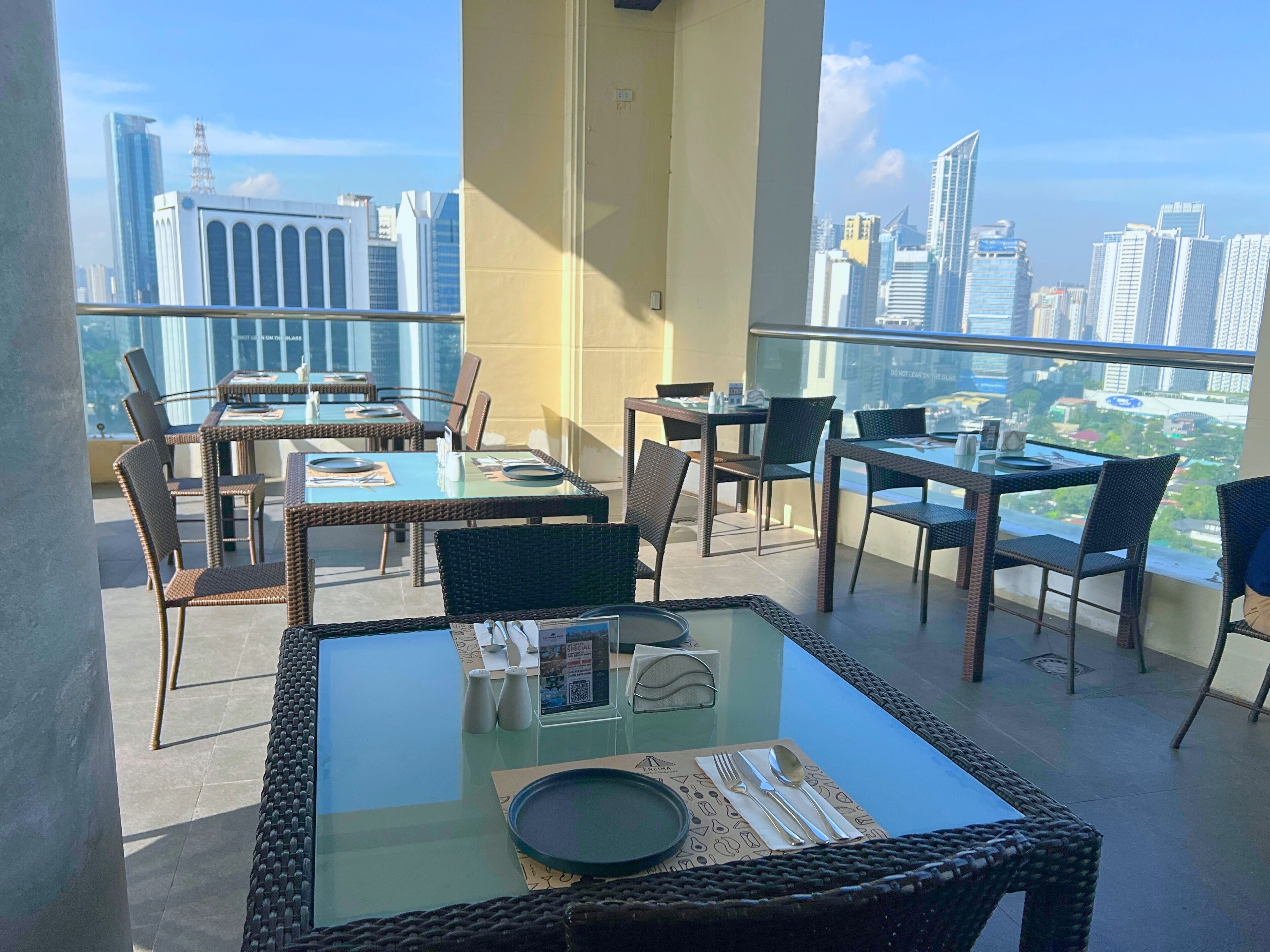A balcony with tables and chairs, a glass-top table, and a view of a cityscape with tall buildings.