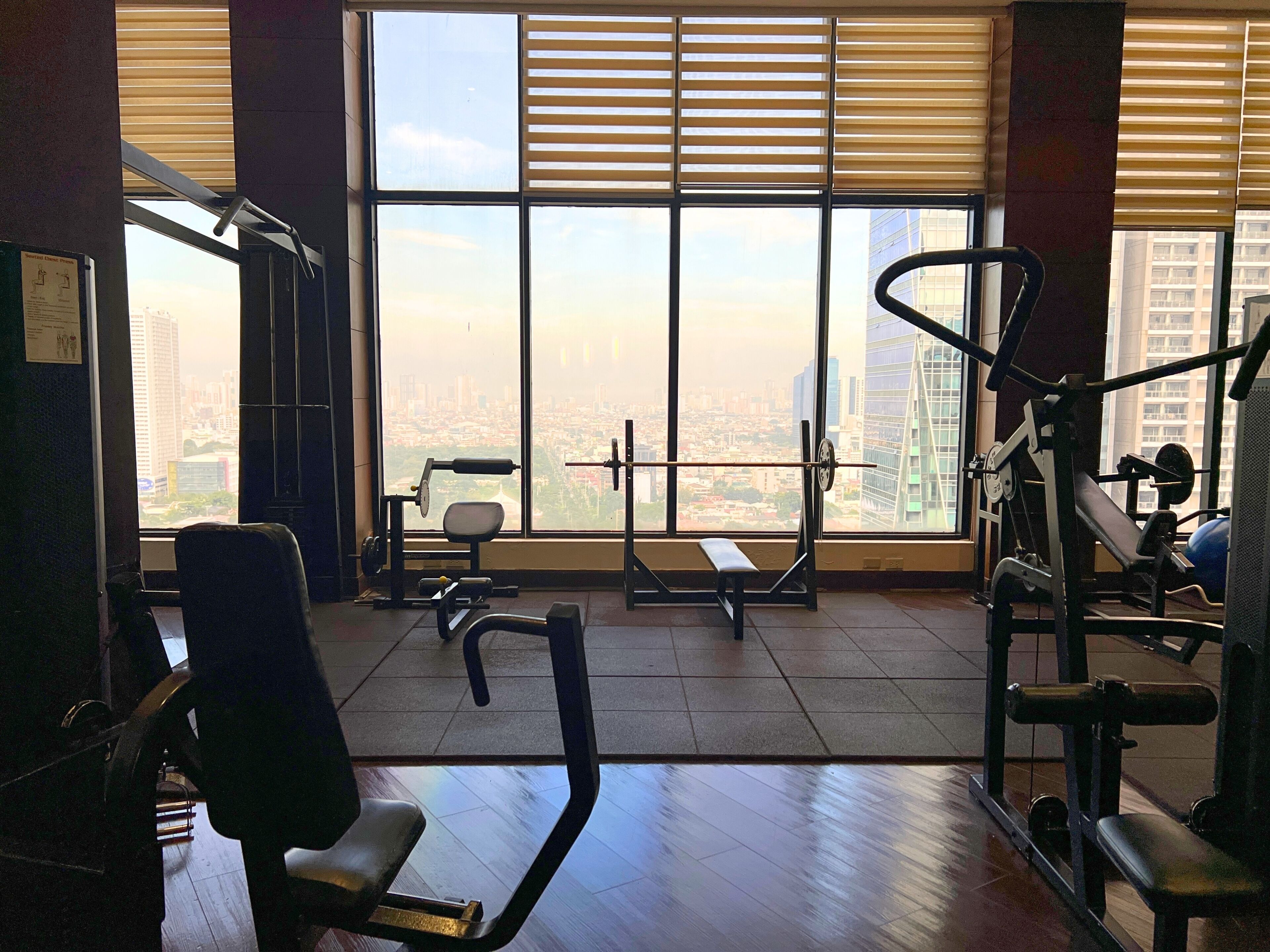 A gym with exercise equipment, large windows, and a view of a cityscape.