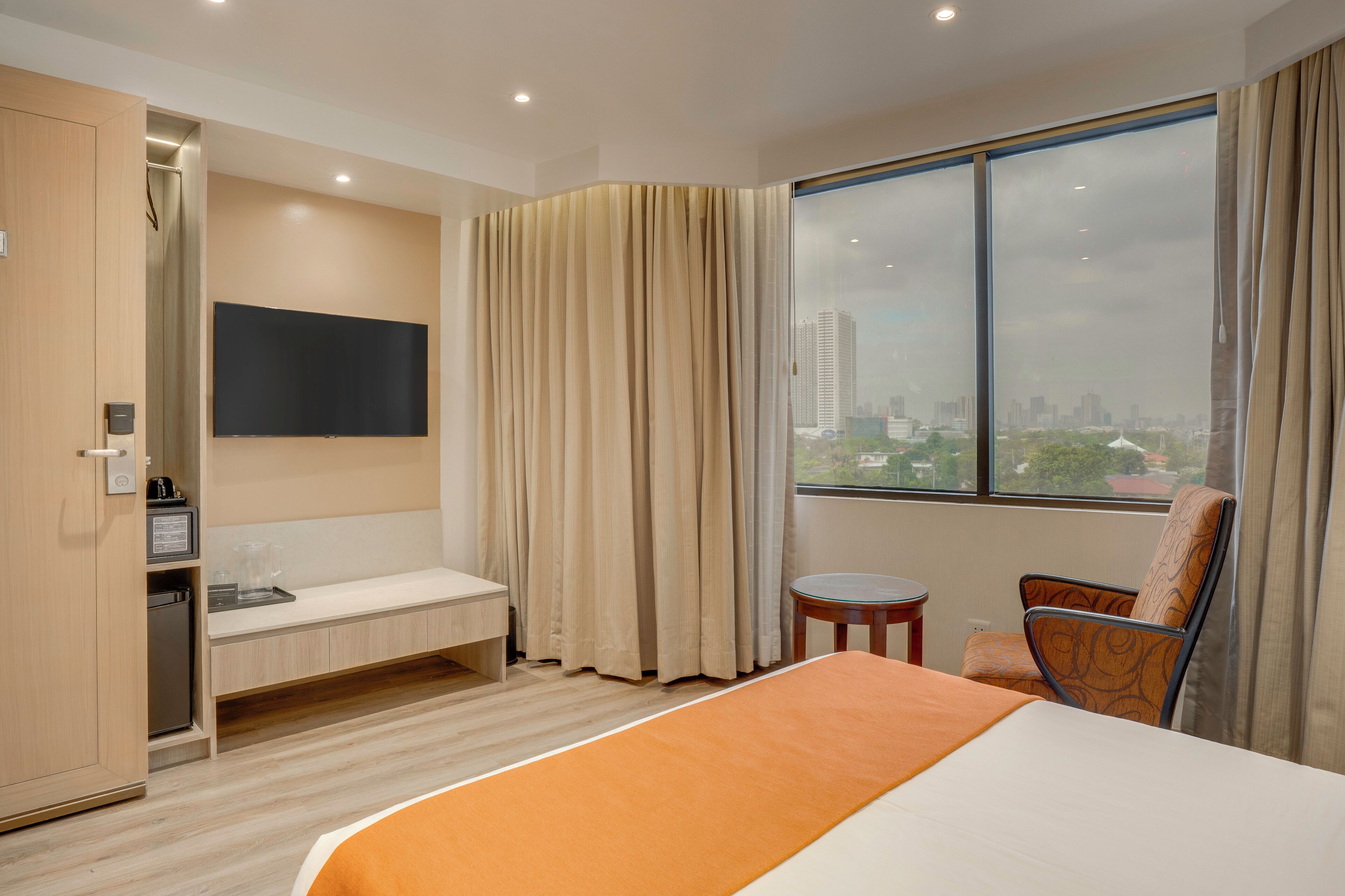 Ein Hotelzimmer mit Bett, Fernseher, Schreibtisch, Stuhl und Blick auf die Stadt.