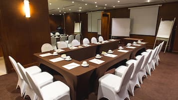 Un salón de conferencias con una larga mesa, sillas blancas y una pizarra.