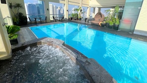 Una piscina en la azotea con agua azul cristalina, rodeada de plantas en macetas y mobiliario de exterior.