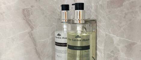 Two bottles of City Garden Hotels bath gel and conditioning shampoo mounted on a marble wall.