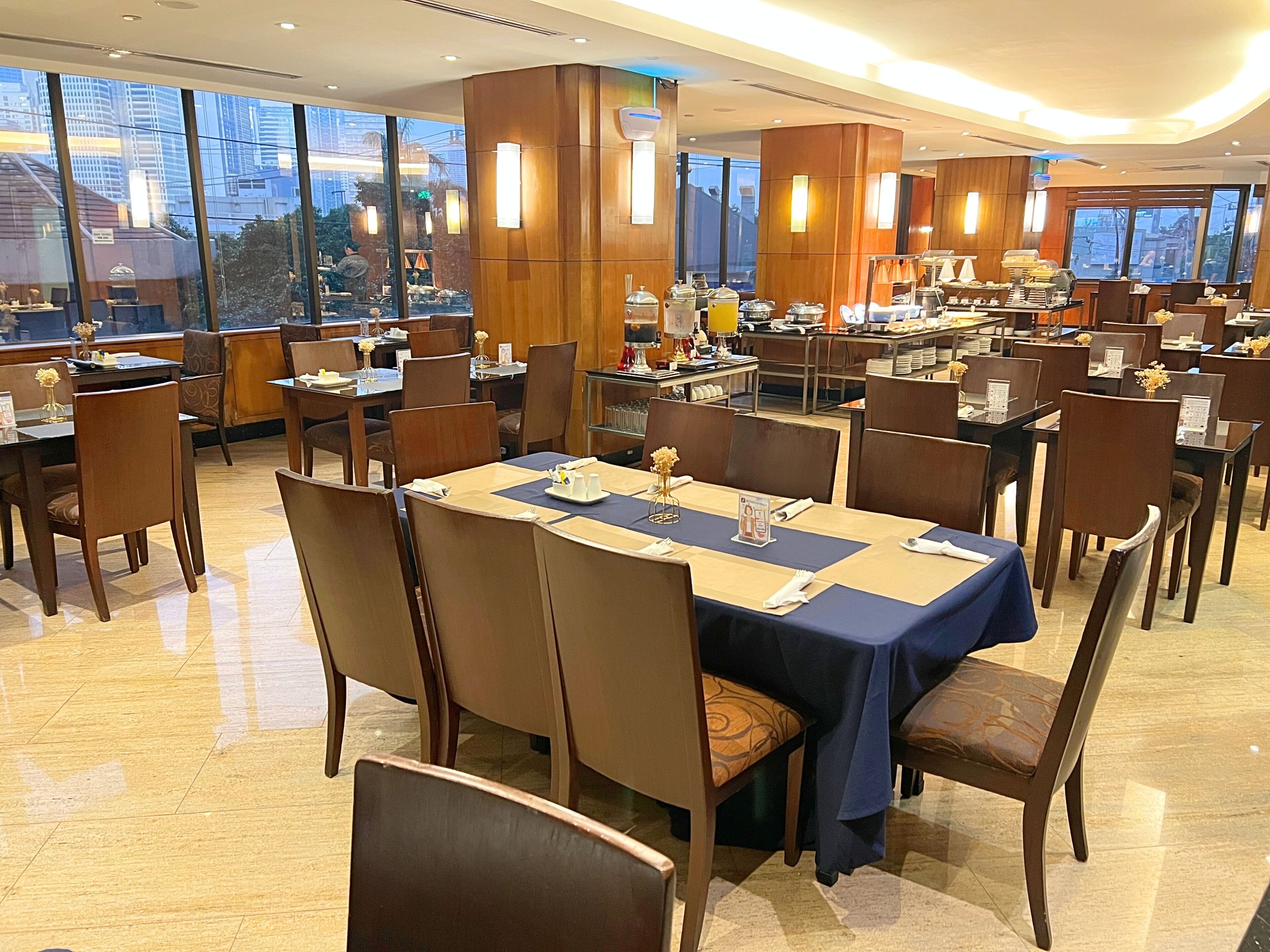 A hotel dining area with multiple tables, chairs, and a buffet setup.