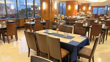 A hotel dining area with multiple tables, chairs, and a buffet setup.