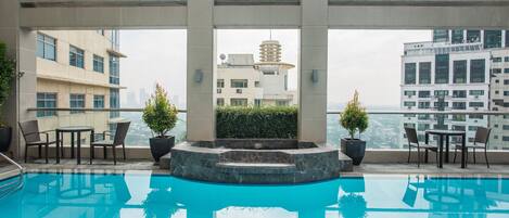 Una piscina en la azotea con vistas despejadas al paisaje urbano, rodeada de edificios modernos y equipada con mobiliario exterior.