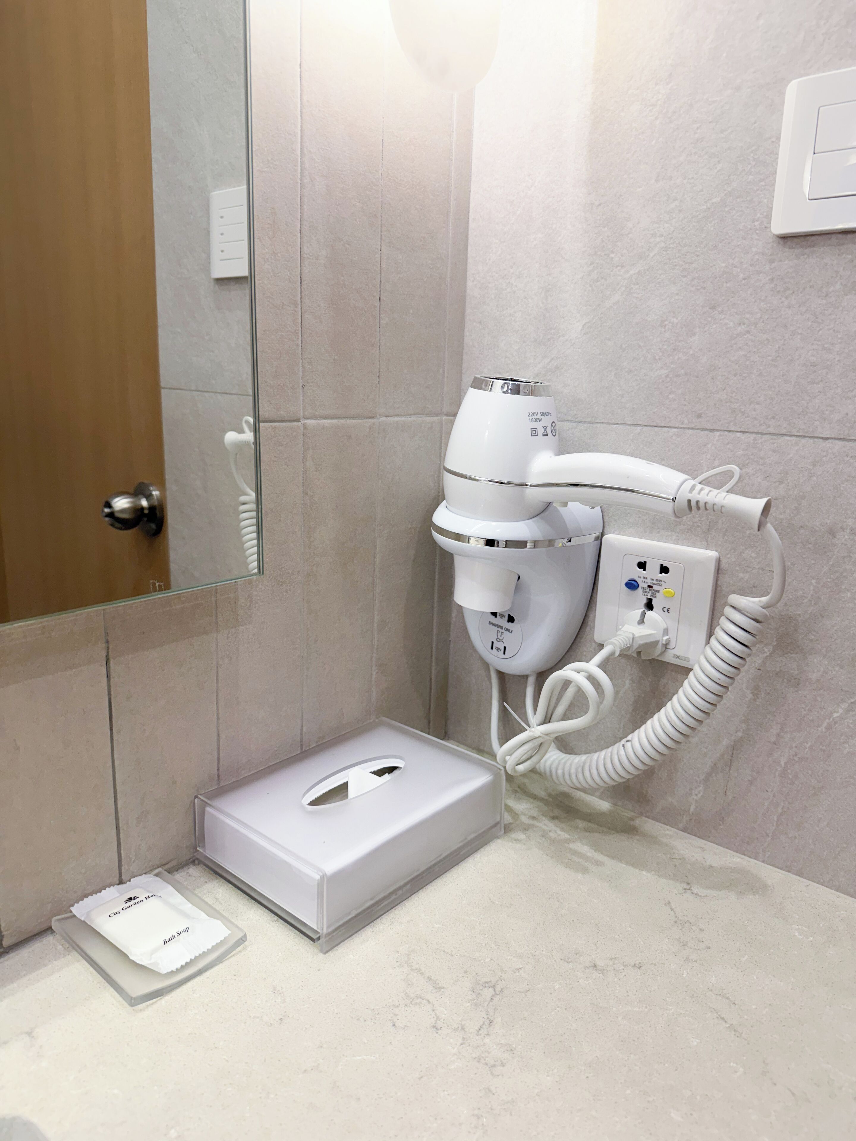A bathroom with a hairdryer mounted on the wall, a tissue box, and a hand dryer on the floor.