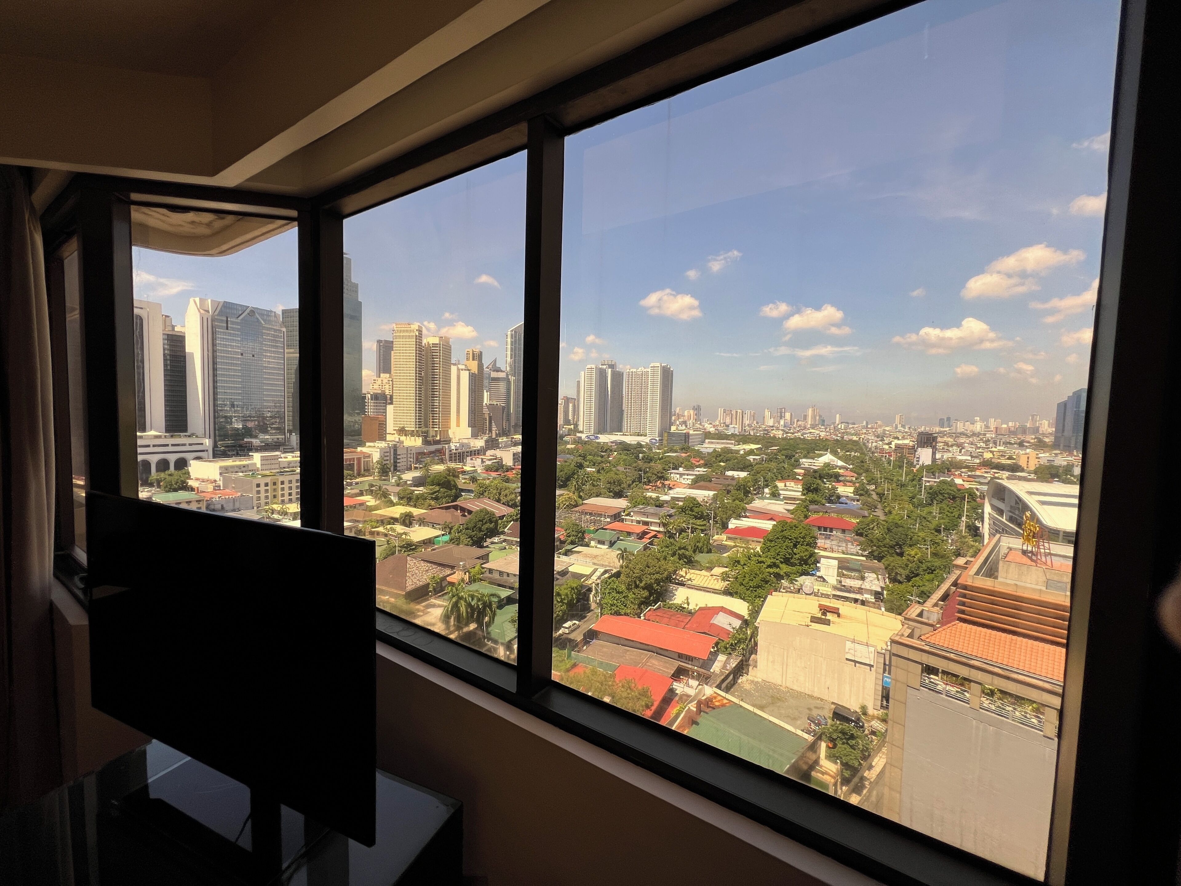 Quarto com uma janela ampla que oferece vista para um horizonte urbano com arranha-céus e uma combinação de edifícios residenciais e comerciais.