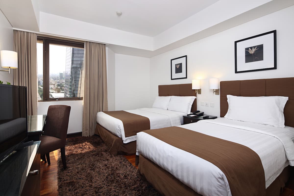 Habitación de hotel con dos camas, televisor, escritorio y vista a la ciudad.