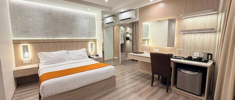 Una habitación de hotel moderna con cama, mesita de noche, escritorio, silla y una kitchenette compacta.