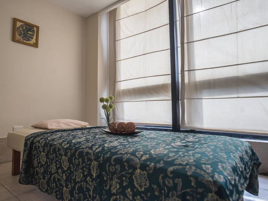 A bedroom with a bed, a window with blinds, a small plant, and a wall-mounted picture.