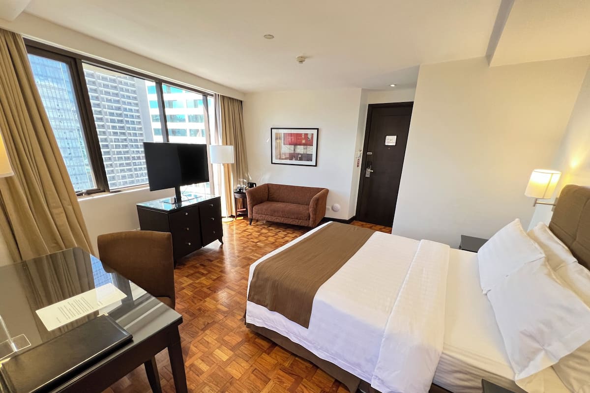 Habitación de hotel con cama, escritorio, silla, sofá, televisión y ventana con vista a la ciudad.