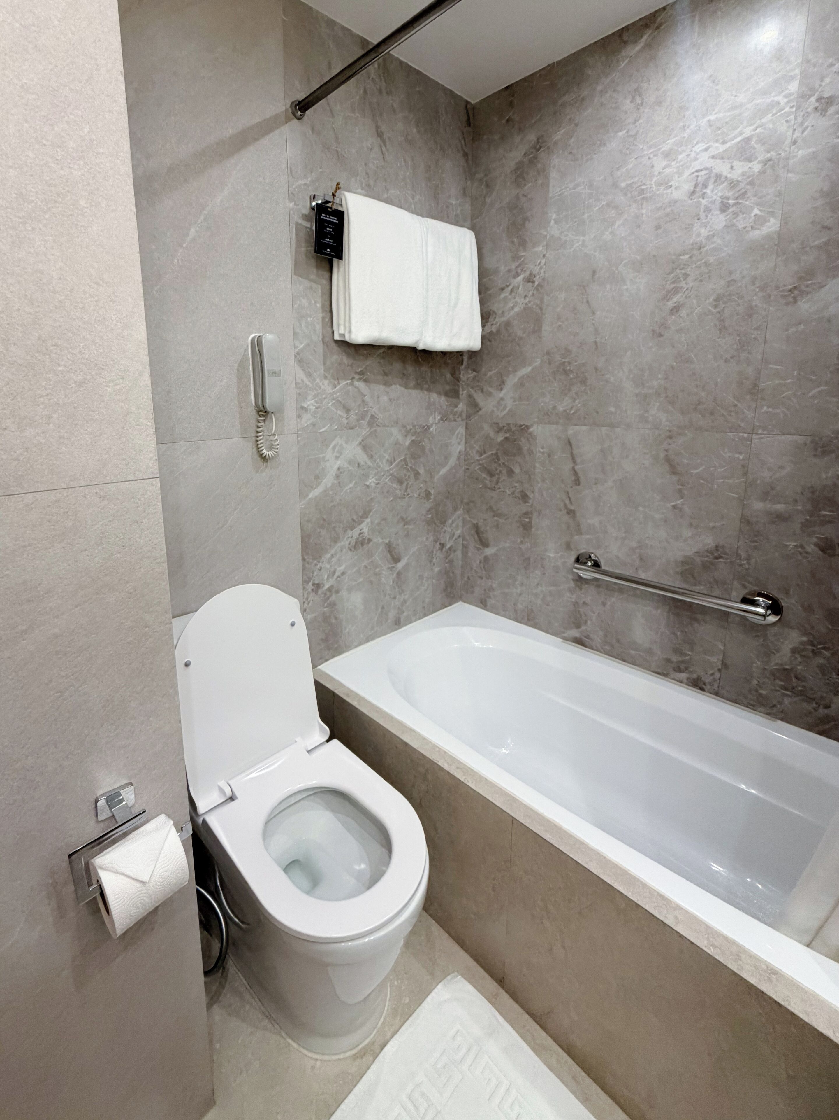 A modern bathroom with a toilet, a bathtub, and a marble wall.