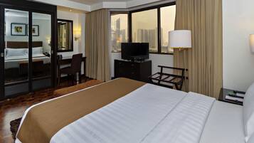 A hotel room with a large bed, a television, a desk, and a view of the cityscape through the window.