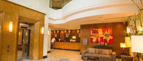 A modern lobby with a reception desk, seating area, and a glass railing overlooking the lower level.