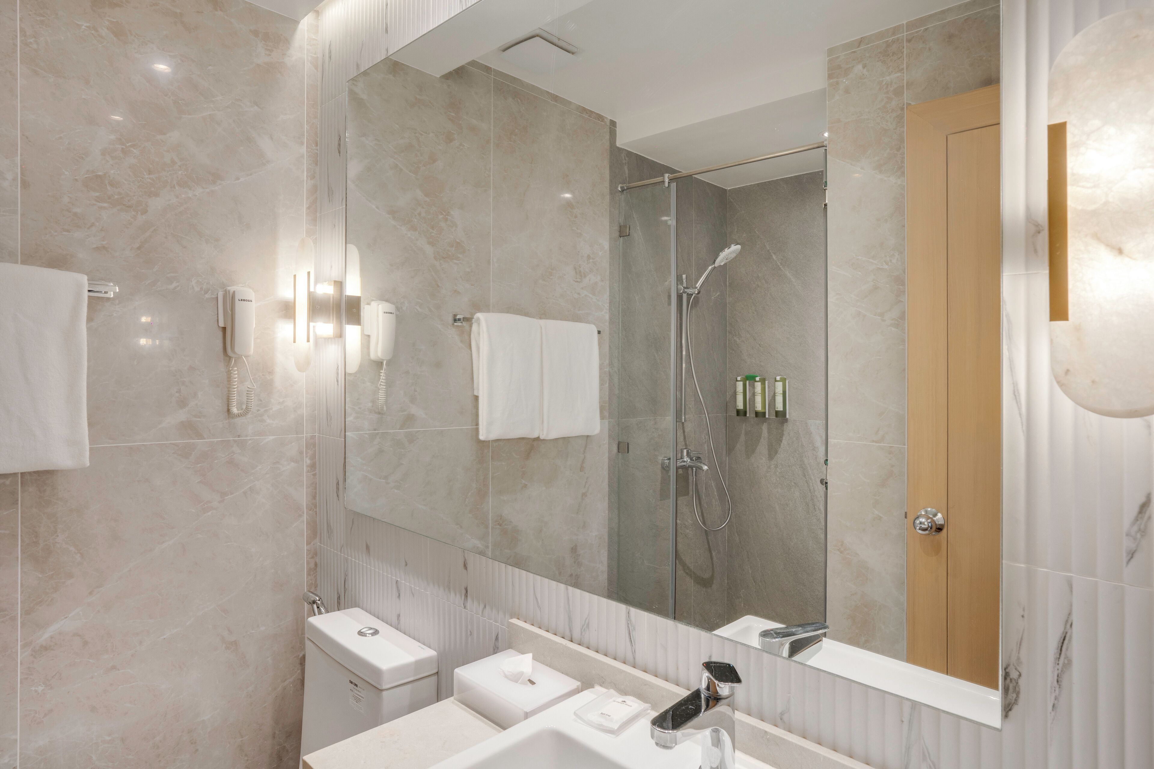 A modern bathroom with a large mirror, a shower, and a toilet.