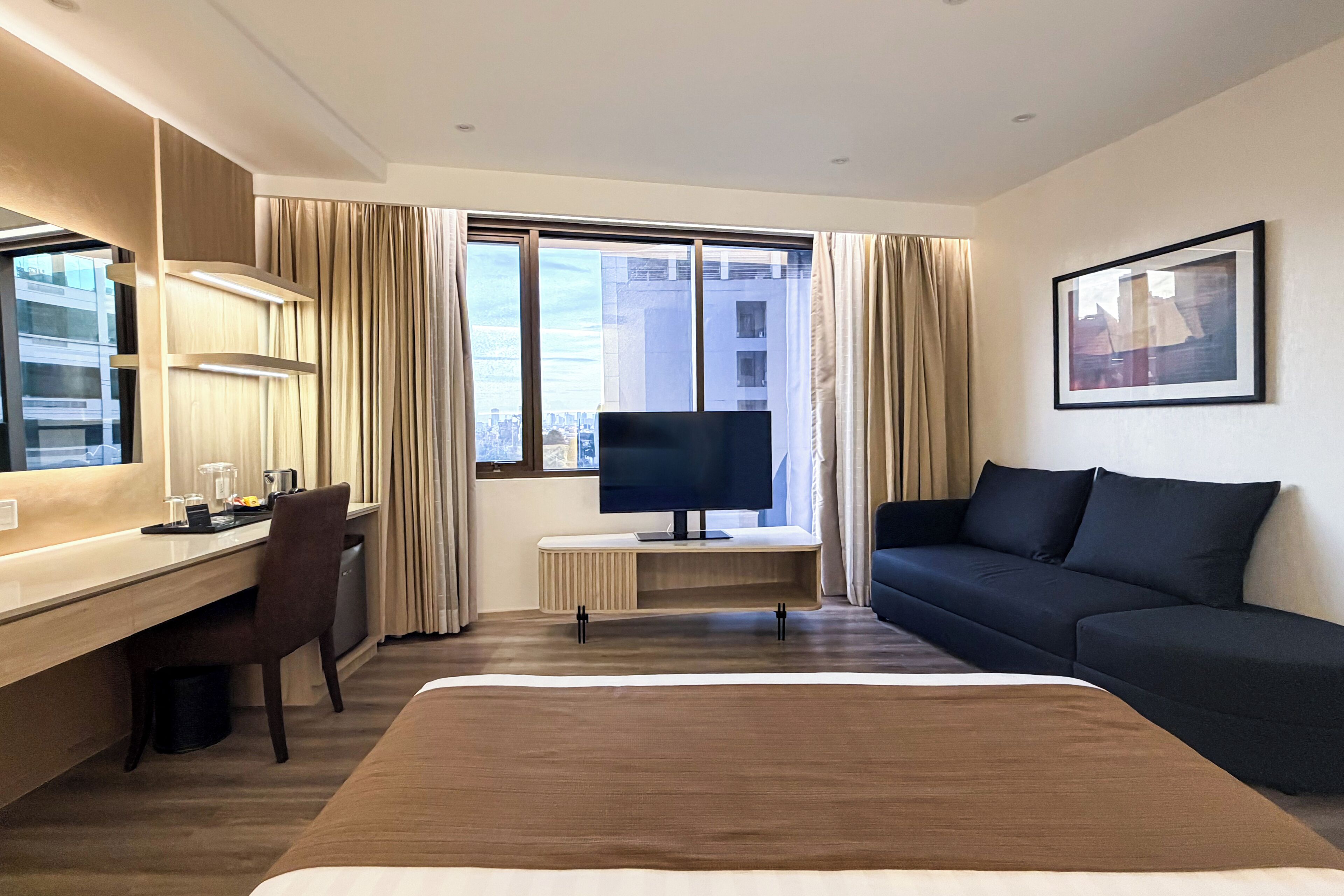 A hotel room with a bed, a desk, a chair, a TV, and a sofa.