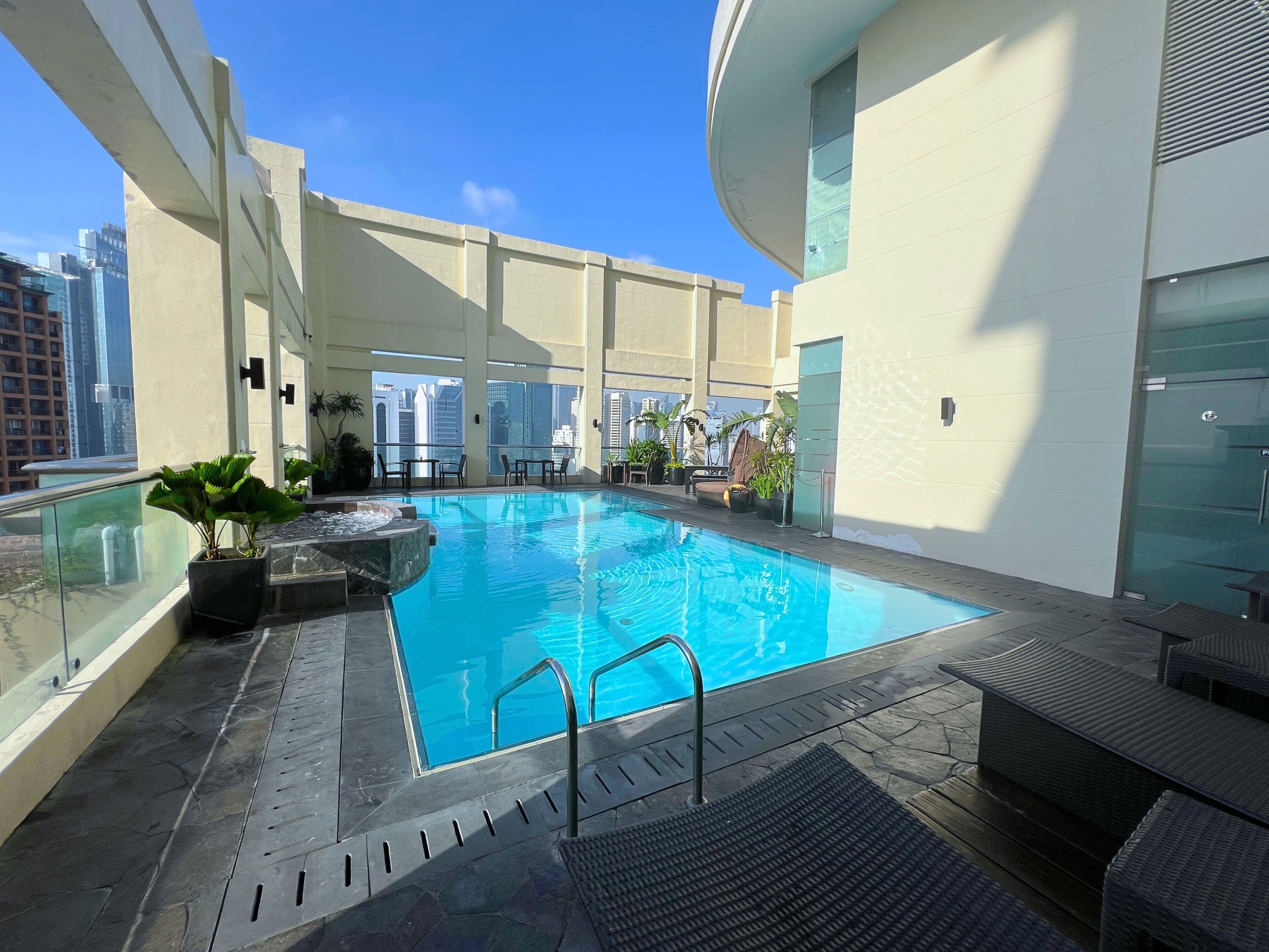 Una piscina en la azotea con agua azul cristalina, rodeada de sillones de descanso y plantas en macetas.