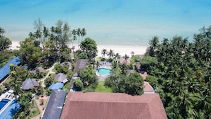 An aerial view of a coastal property with a swimming pool, beach, and palm trees.