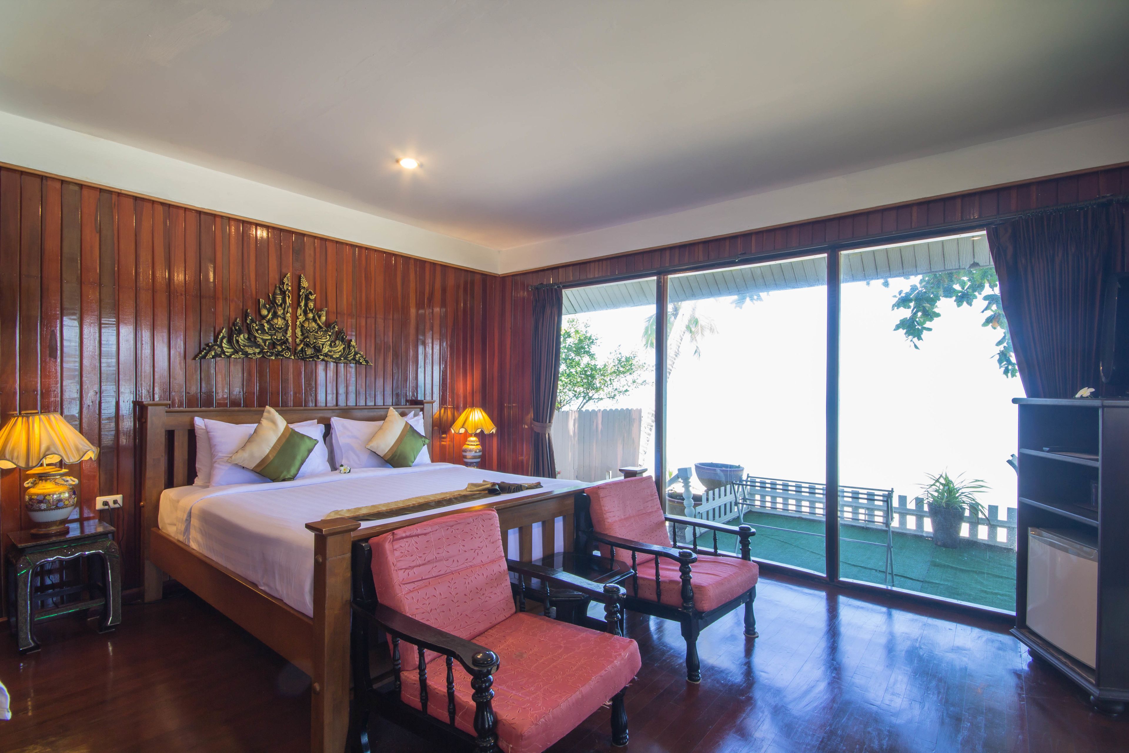 A bedroom with a large bed, two chairs, a nightstand, and a window with a view of the outdoors.