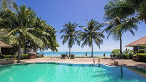 A clear blue pool surrounded by palm trees and lounge chairs, with a view of the ocean.