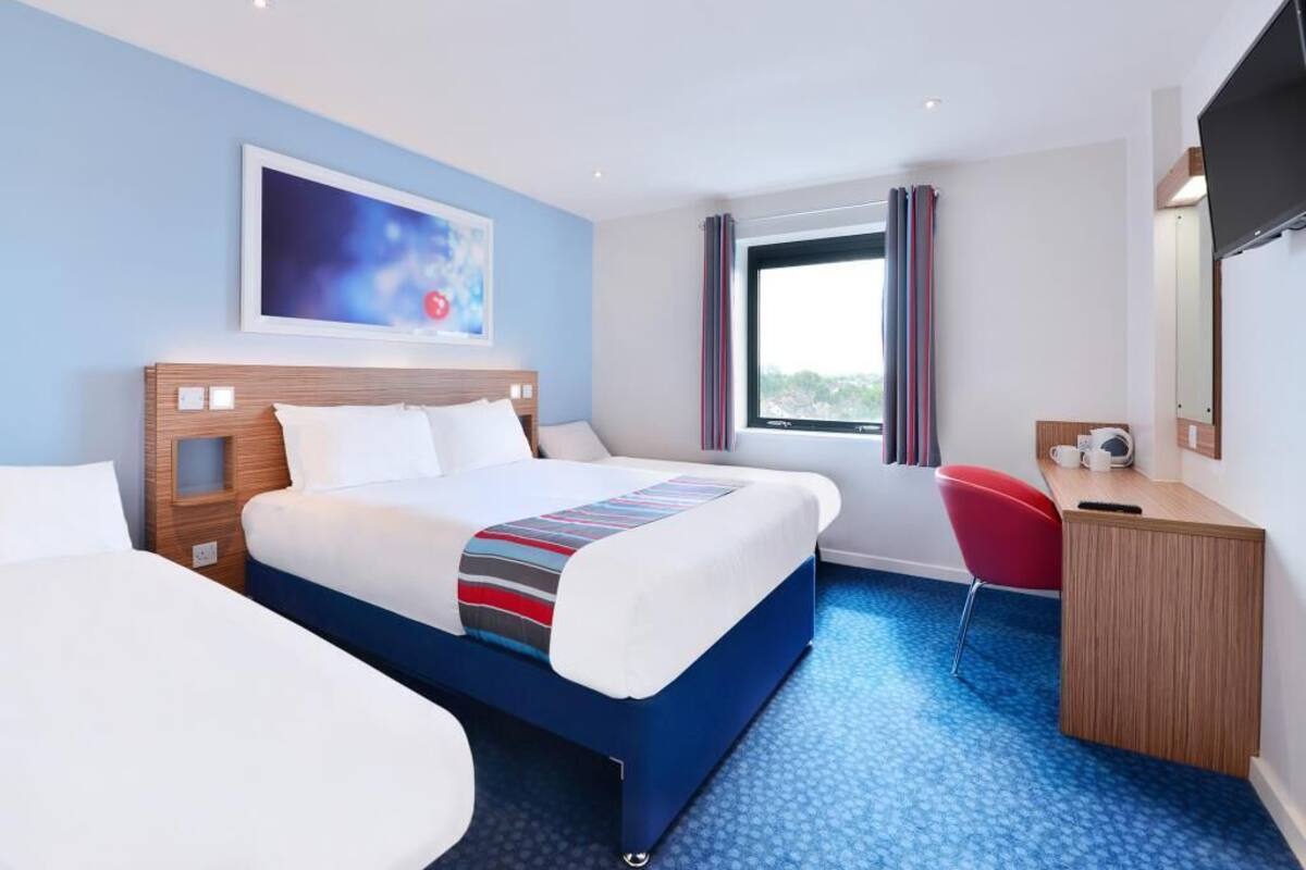 Ein Hotelzimmer mit zwei Betten, einem Schreibtisch, einem Stuhl, einem Fernseher und einem Fenster mit Vorhängen.