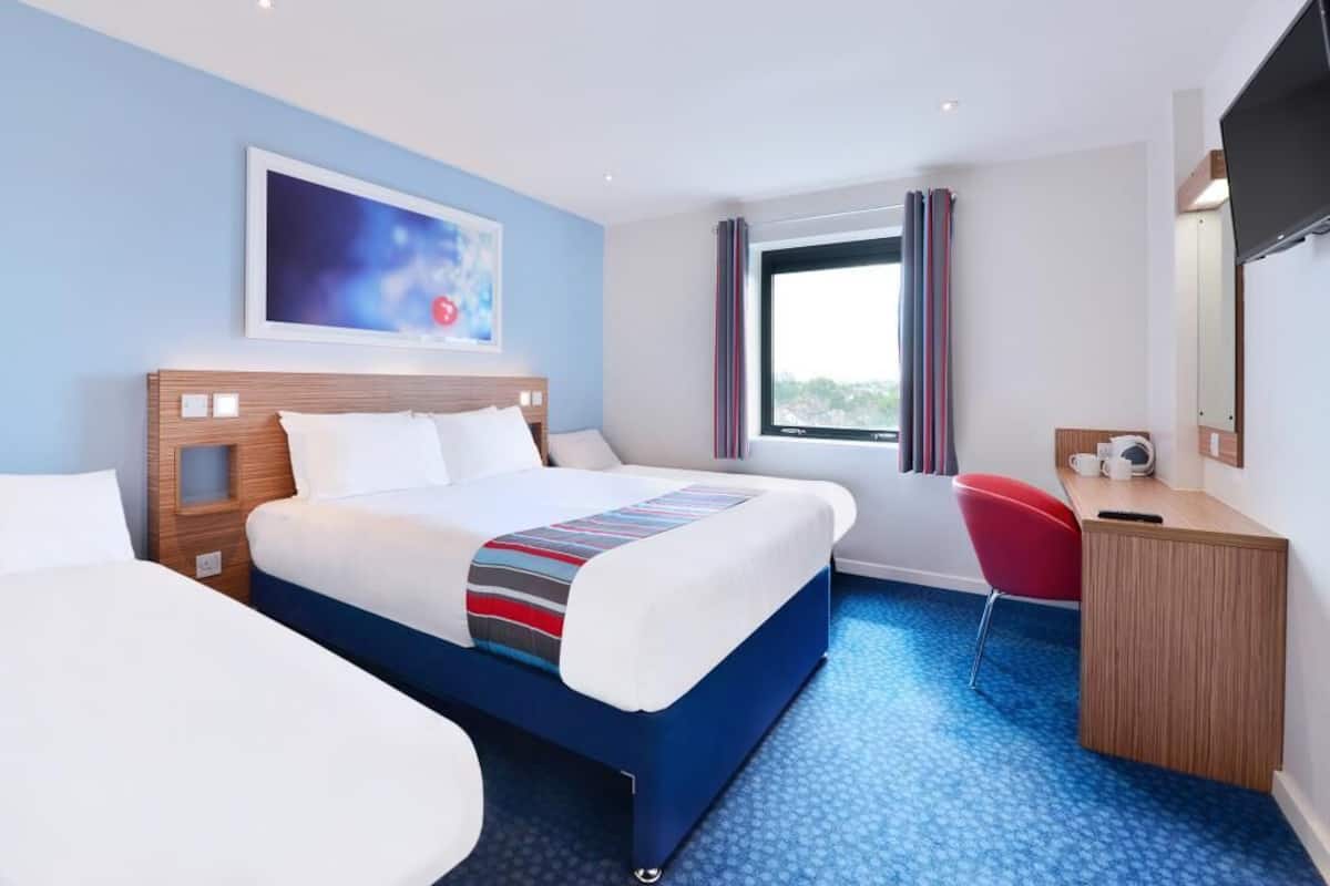 A hotel room with a large bed, a desk, a chair, a TV, and a window with curtains.