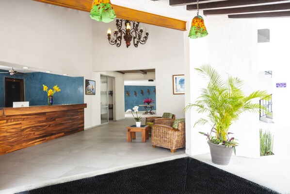 A reception area with a wooden reception desk, a chandelier, wicker furniture, and potted plants.