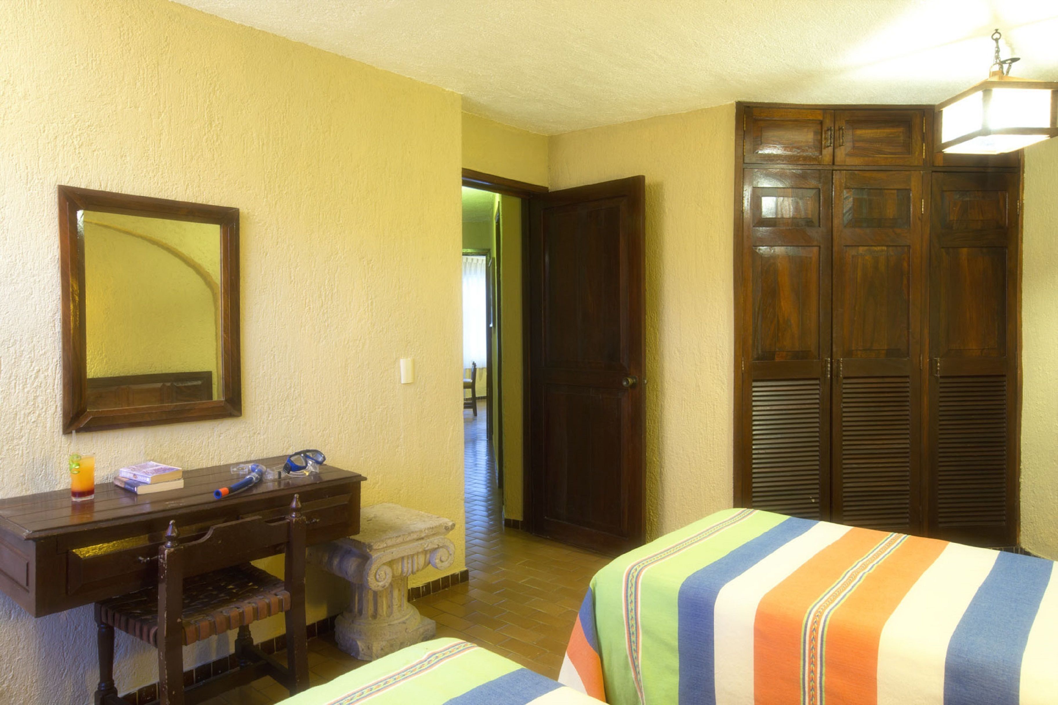 A hotel room with a wooden desk, a bed with striped bedding, and a large mirror on the wall.