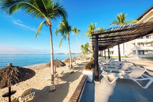 A beachside resort with sun loungers, palm trees, and a clear view of the ocean.