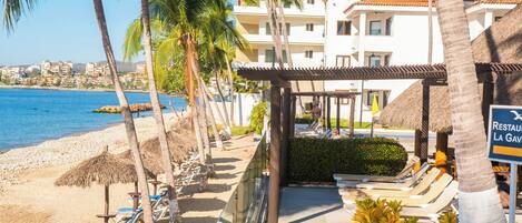 Un hôtel situé en bord de mer, agrémenté de palmiers, de chaises longues et d’un espace piscine.