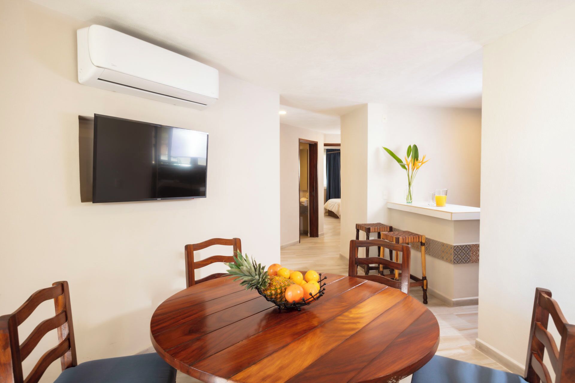 Un comedor con una mesa de madera, sillas y un frutero. Un televisor de pantalla plana está montado en la pared.