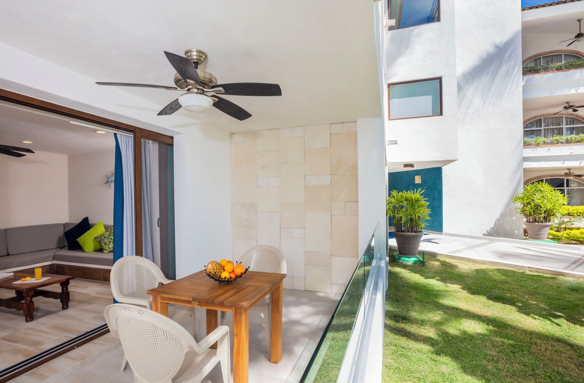 A modern apartment with a dining area, a ceiling fan, a balcony with potted plants, and a view of the building's exterior.