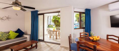 A dining area with a wooden table and chairs, a ceiling fan, and a view of a pool and greenery outside.
