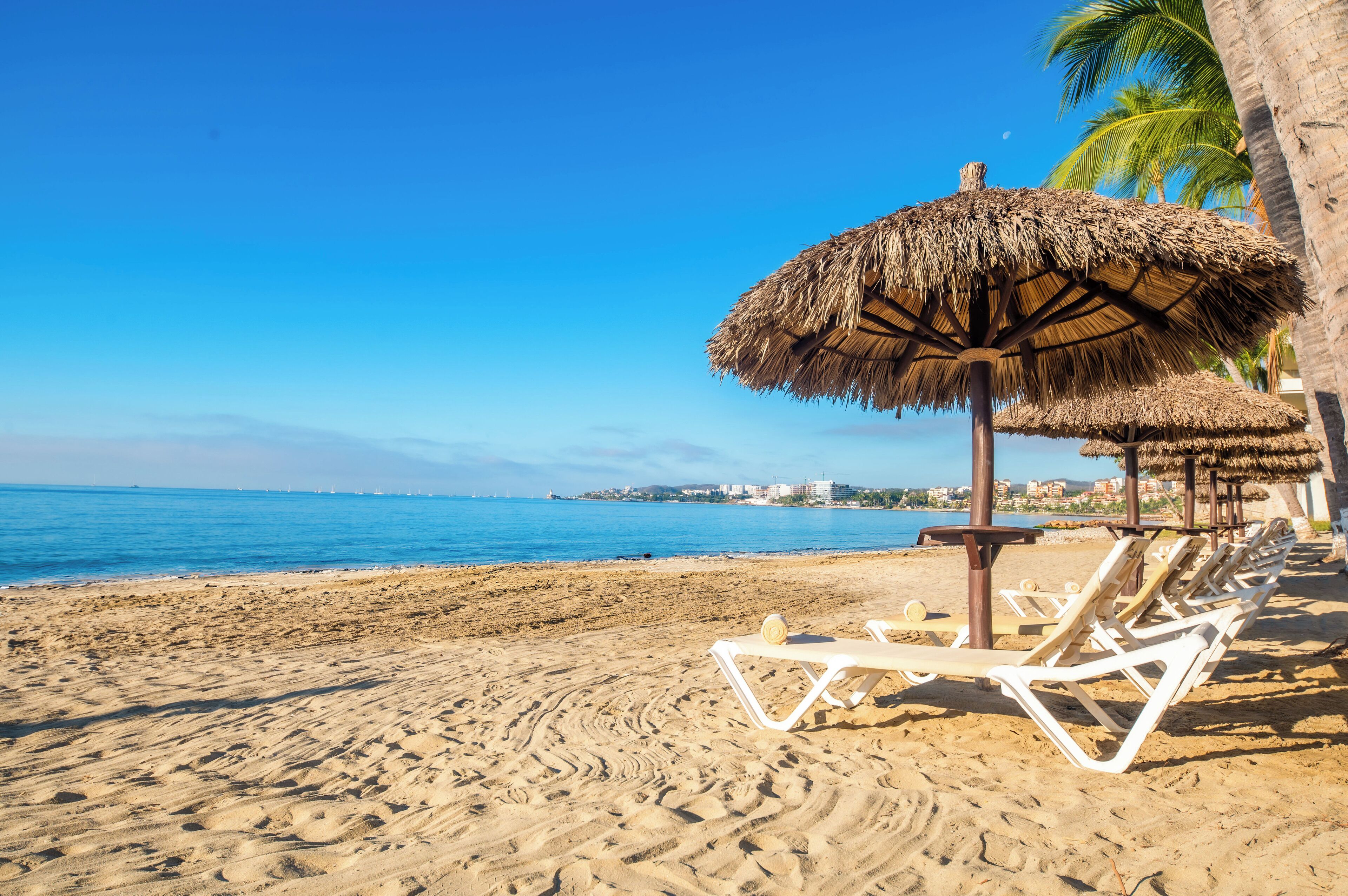 Une plage avec des parasols en chaume et des chaises longues.