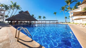 A clear blue pool with a thatched-roof structure and palm trees in the background. - Vista Vallarta All Suites on the Beach (Bucerías)