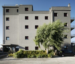 A multi-story building with a flat facade, numerous windows, and a parking area in front. - Best Western Hotel Corsi (Fiumicino)