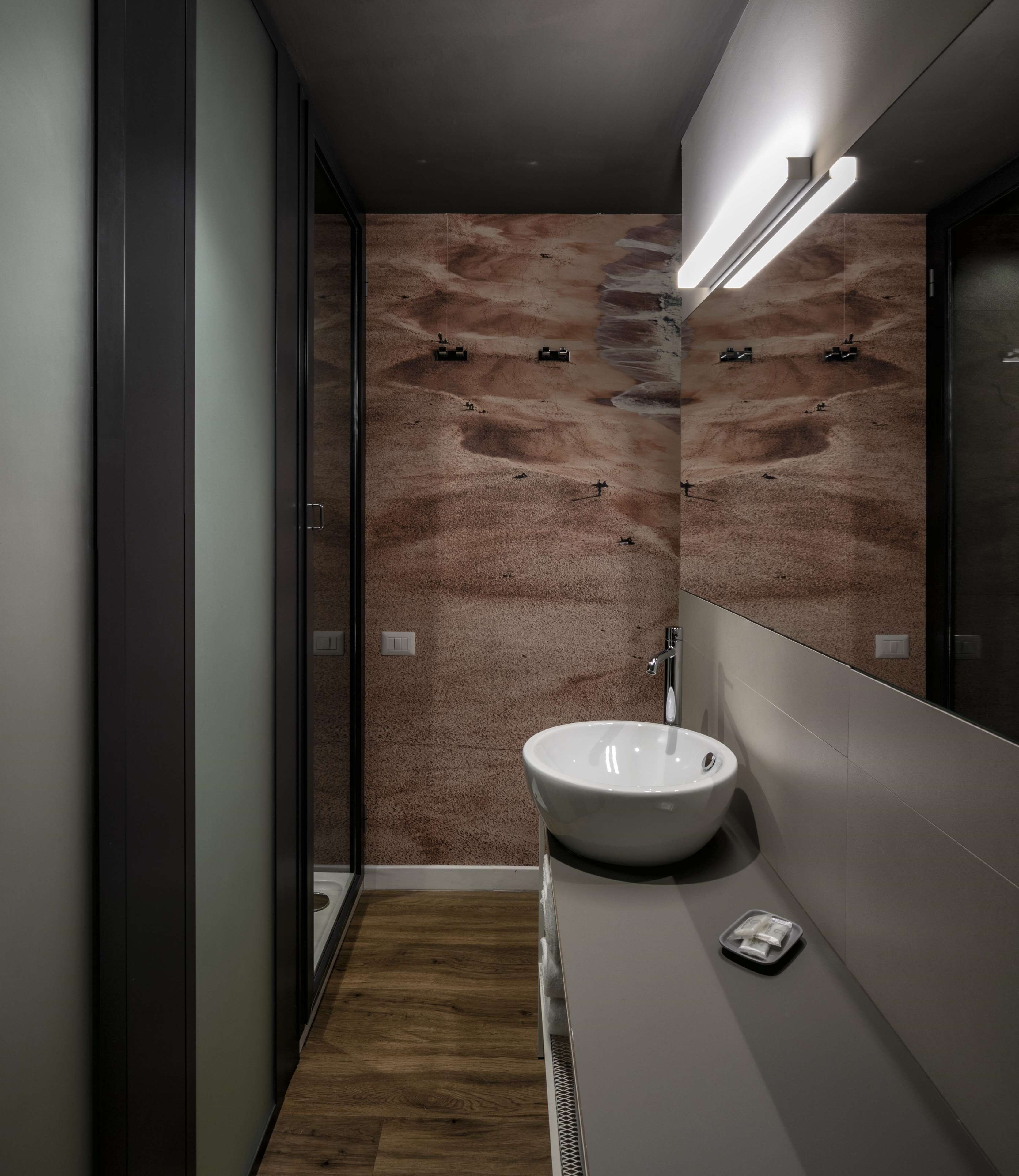 Ein modernes Badezimmer mit einem großen Spiegel, einem weißen Waschbecken und einer strukturierten Wand.