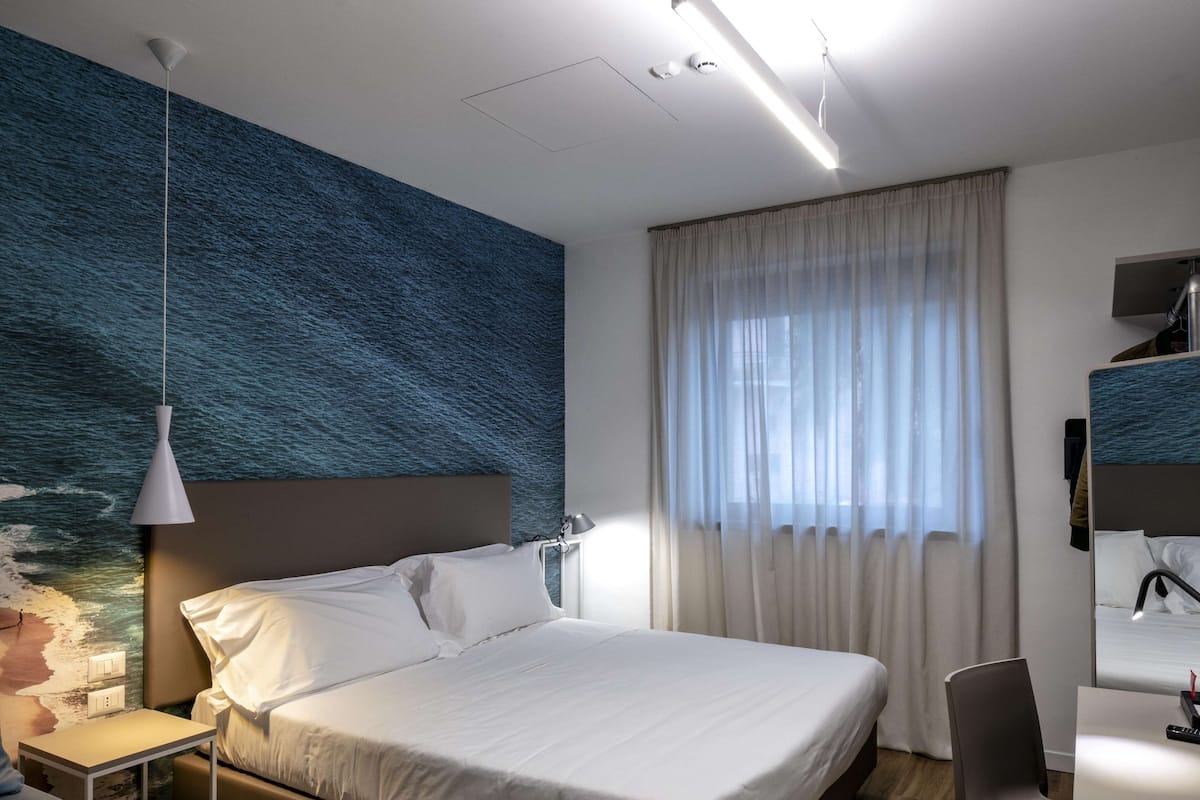A modern hotel room with a large bed, a desk, and a chair.