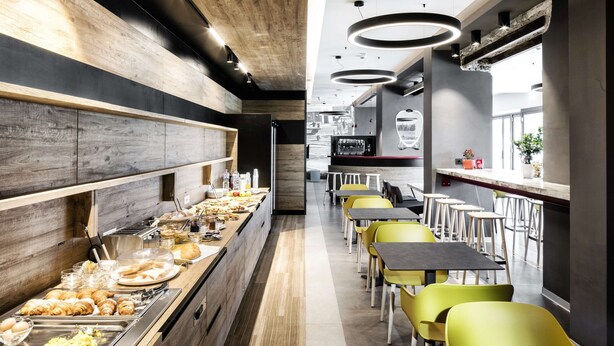 A modern cafeteria with a long counter, various food options, and bright yellow chairs. - Best Western Hotel Corsi (Fiumicino)