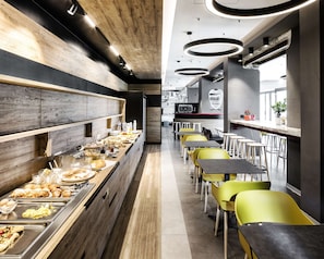 Una cafetería moderna con una barra larga, diversas opciones de comida y sillas de color amarillo brillante.
