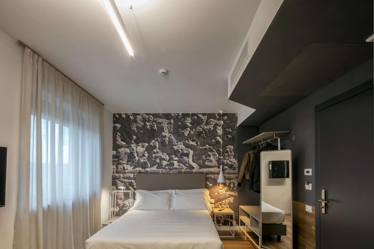 A modern bedroom with a large bed, a wardrobe, a vanity, and a stone-patterned wall.