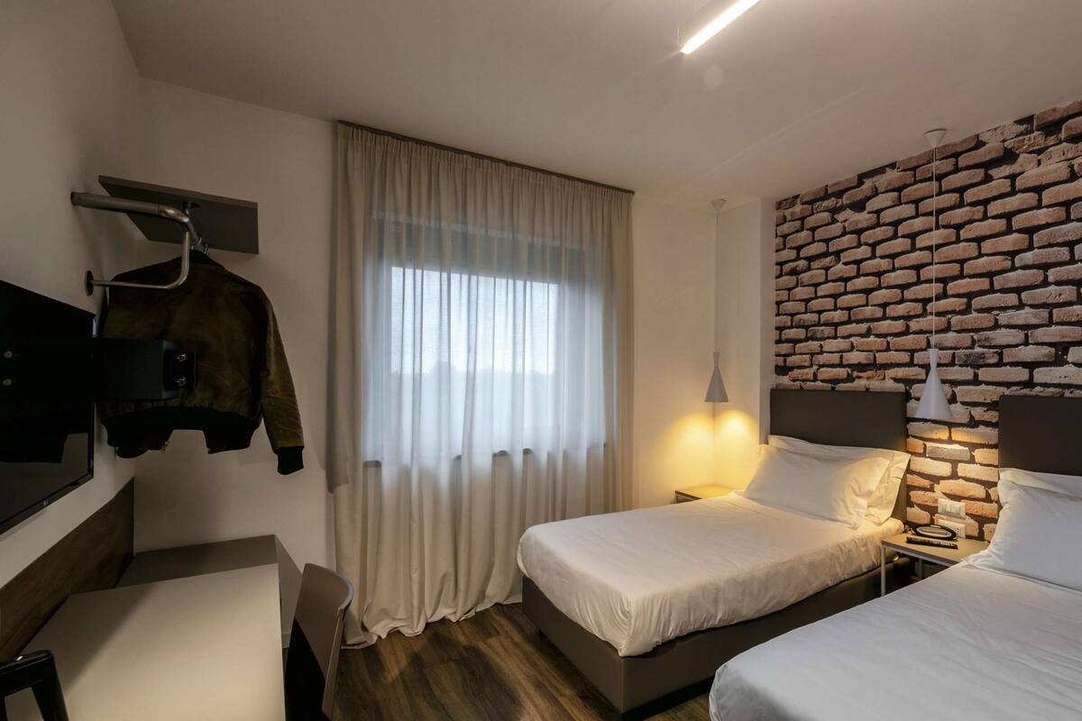 A hotel room with two beds, a brick wall, a TV, and a coat rack.