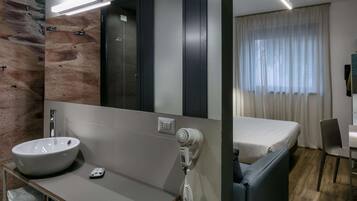 A modern hotel room with a large mirror, a sink, a hairdryer, a bed, and a window with curtains.