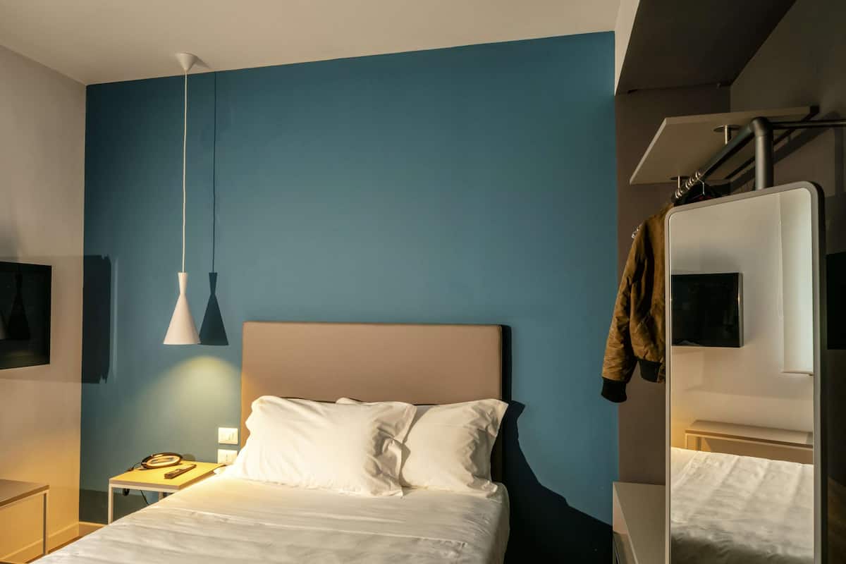 A modern hotel room with a bed, a nightstand, a lamp, and a mirror.