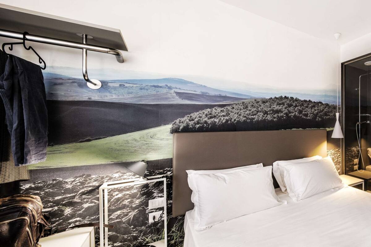 A modern hotel room with a bed, a wardrobe, and a large window with a scenic view.