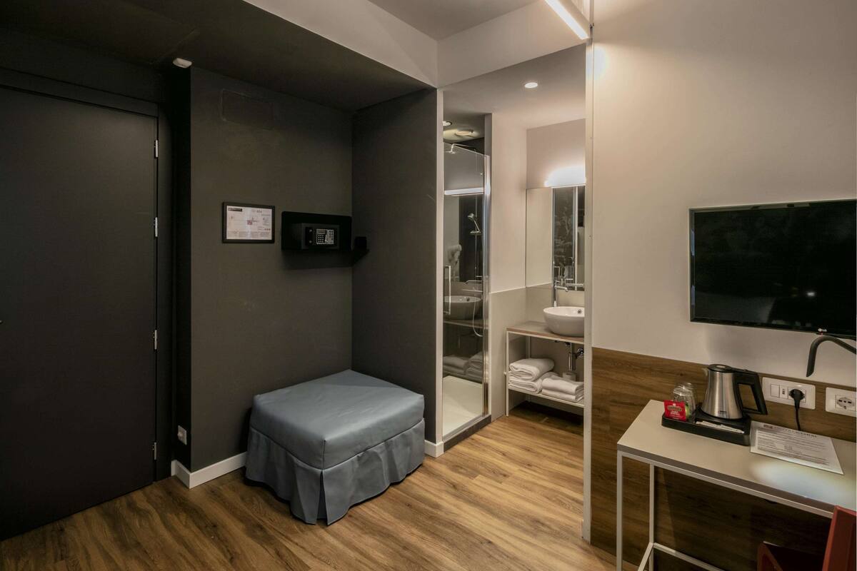 A compact hotel room with a wooden floor, a small seating area, a sink, and a television.