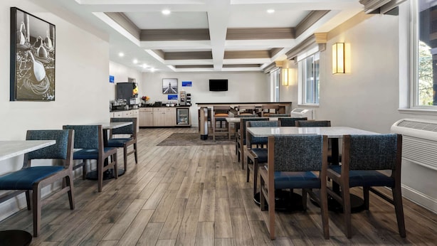 A modern restaurant with wooden flooring, blue upholstered chairs, and a central island with a counter.