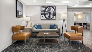 A modern hotel lobby with a sofa, two leather chairs, a coffee table, and artwork on the walls.