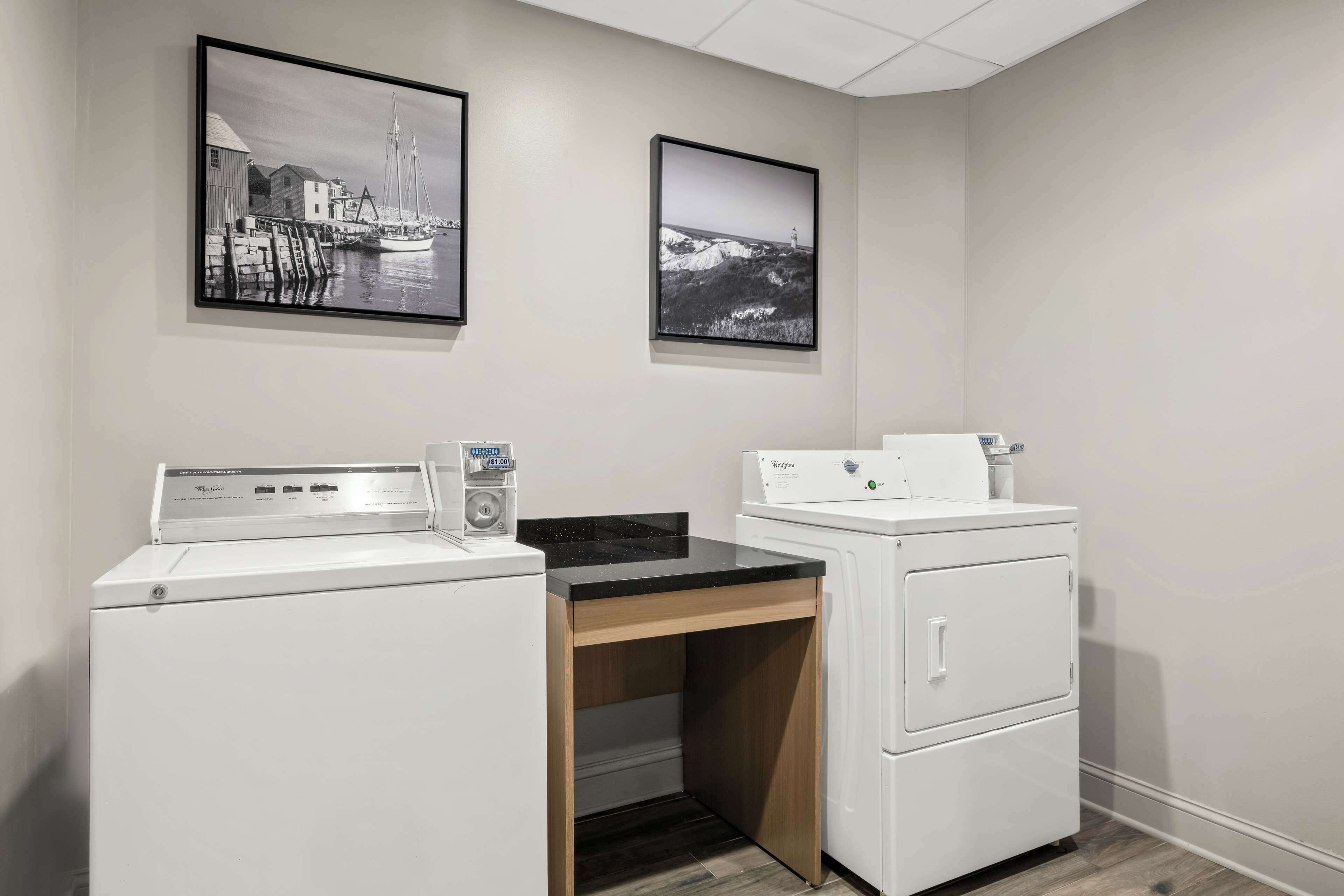 A laundry room with two white washers and dryers, a wooden desk, and two black-and-white photographs on the wall.