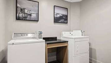 A laundry room with two white washers and dryers, a wooden desk, and two black-and-white photographs on the wall.
